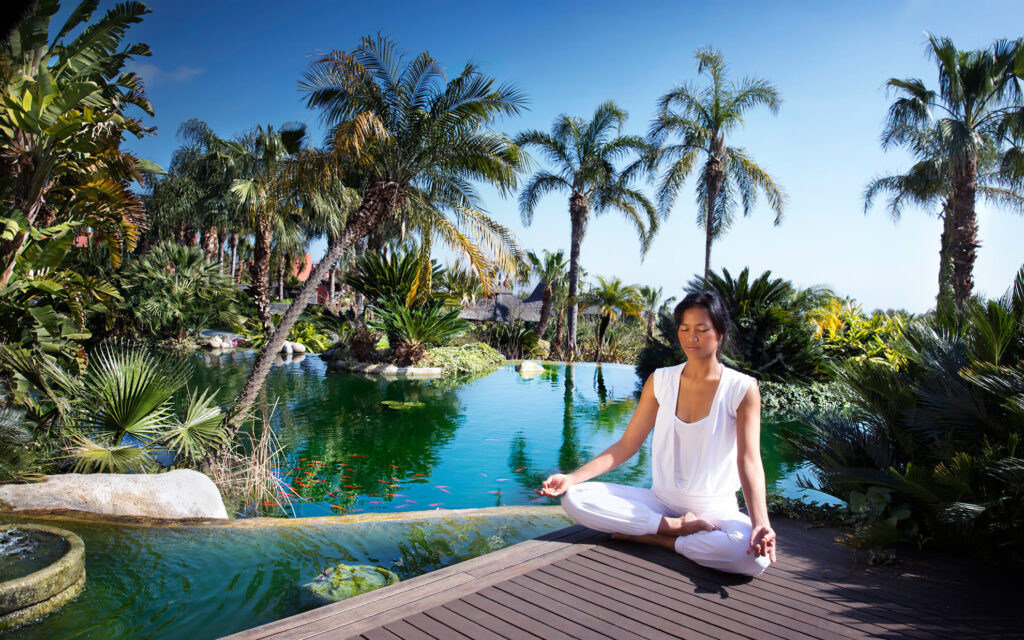 Woman meditating by the lagoon at Asia Gardens Hotel & Thai Spa surrounded by palm trees